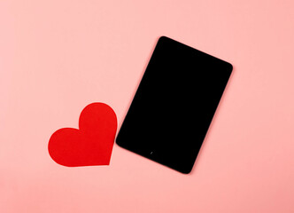 composition of a red heart near a gadget tablet on a pink background, concept of love, dating or...