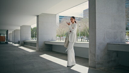 Business woman recording voice message standing on office parking sunny day. 