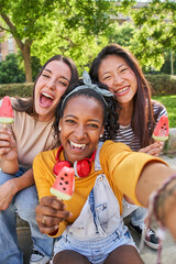 Vertical Selfie of three smiling young multi-ethnic women outdoors eating ice cream. Friends having...