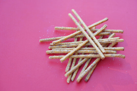 Crunchy salty and spicy flavored pretzel sticks, breadsticks, snacks on red background. Concept, junk food, appetizer.          