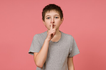 Little boy gray T-shirt on pink background urges to observe silence