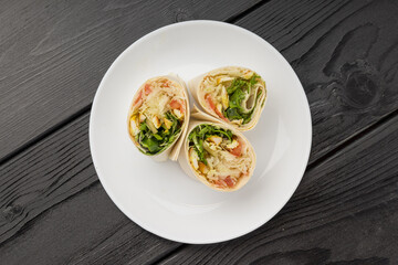A white plate with two halves of a wrap showing chicken, microgreens, and sauerkraut.