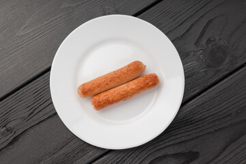 Two grilled sausages on a white plate against a dark wooden background.