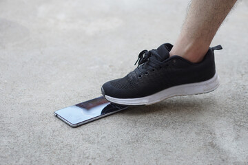 Closeup man wear black shoe, step on smartphone on ground, cause it crack. Concept, damage with...