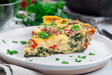 Piece of egg frittata with spinach, roasted peppers, mushrooms, cheese, on plate, horizontal closeup