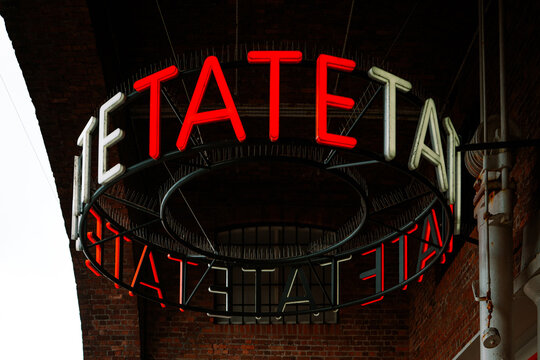 Liverpool, UK - October 10 2023 : The Tate Art Gallery circular sign is lit up in a bright red and white underneath the historic stone arches in the Albert Dock. Famous Modern Art Gallery in Britain