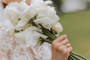 The bride is holding a wedding bouquet of white flowers roses, close-up photo. Wedding details....
