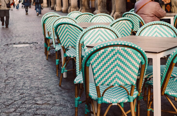 Pale green color chairs on cafe, restaurant terrace. Empty seats, tables on the old town street. Furniture outdoors. People walking. Romantic place.
