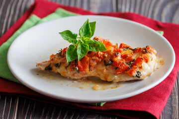 Grilled chicken breast with tomato and mozzarella cheese on it. On plate on wooden table with red and green napkins