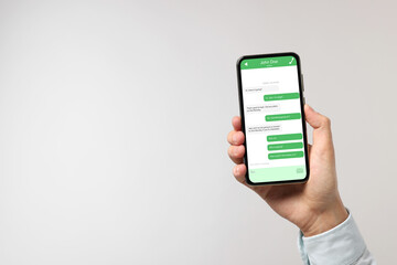 Man texting with friend using messaging application on smartphone against light grey background, closeup. Space for text