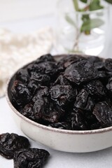 Bowl with sweet dried prunes on light table, closeup