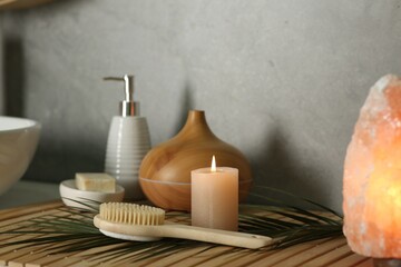Fototapeta na wymiar Composition with different spa products, burning candle and Himalayan salt lamp on countertop in bathroom