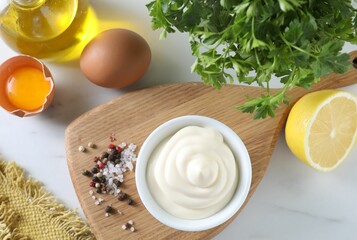 Tasty mayonnaise sauce in bowl, ingredients and spices on white table, flat lay