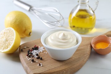 Tasty mayonnaise sauce in bowl, ingredients and spices on white table, closeup