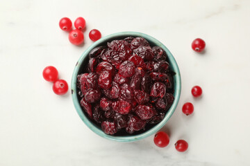 Tasty dried cranberries in bowl and fresh ones on white table, top view