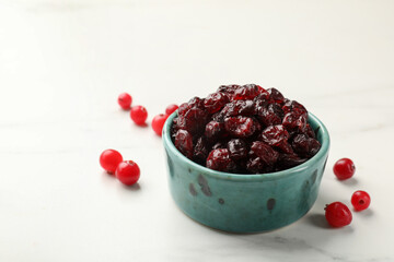 Tasty dried cranberries in bowl and fresh ones on white marble table, closeup. Space for text