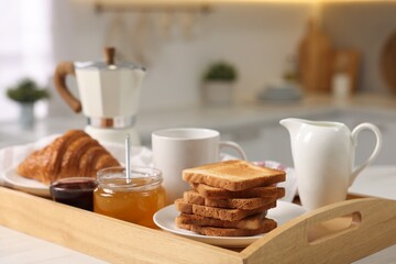 Breakfast served in kitchen. Tray with toasts, honey, jam, fresh croissant, coffee and pitcher of...