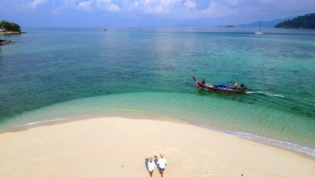 a couple of men and women walking at a white sandbank beach in the ocean of Koh Lipe Island Southern Thailand, with turqouse colored ocean and white sandy beach sandbar at Ko Lipe.