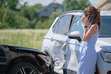 Stressed driver talking on sellphone on roadside near her smashed vehicle calling for emergency...