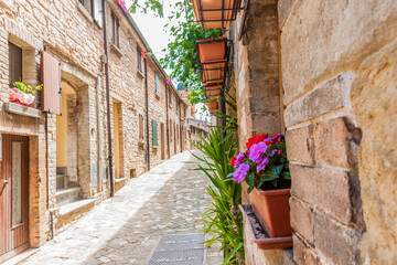 Fototapeta na wymiar Sun shining on one side of narrow cobblestone street lined by typical European stone block residential with colourful potted flowers.