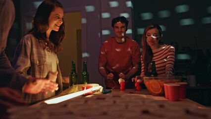 Students playing beer pong at home party with flashing lights. People hangout