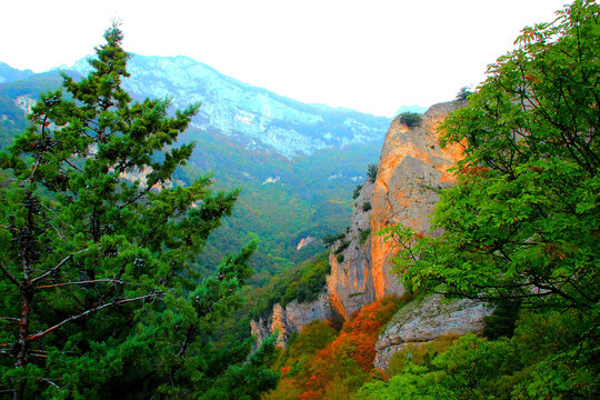 Picture-perfect view at Eremo di Soffiano near Sarnano in the Sibillini Mountains, stretching from the blue-tinted hazy ridges in the background to the reddish and orange rockface and trees in front