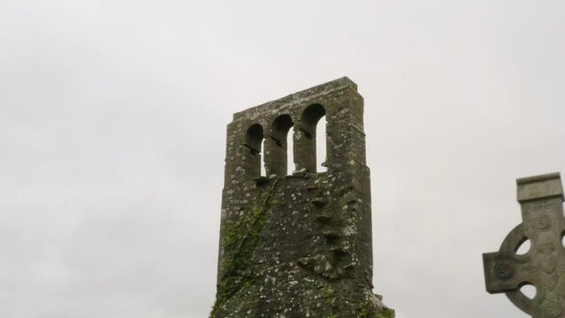 Moss lichen covered church tower and arch windows with eerie old graveyard headstones