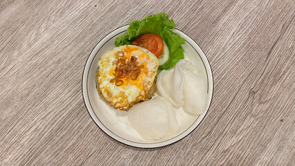 Homemade Fried rice topped with fried egg on skillet, vegetables, and crackers. Isolated on wood table and white plate.