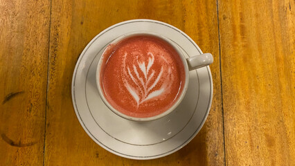 Cup of red velvet latte with leaf shape on old wooden background. White cup