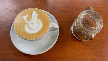 Cup of coffee latte with swan shape on old wooden background. White cup of Banyuwangi coffee bean