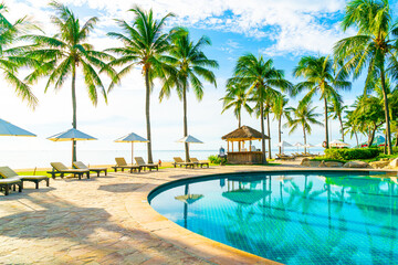 Beautiful luxury umbrella and chair around outdoor swimming pool in hotel and resort with coconut palm tree on blue sky