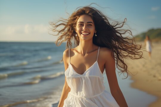 Young happy woman in a white fluttering dress walks on the beach