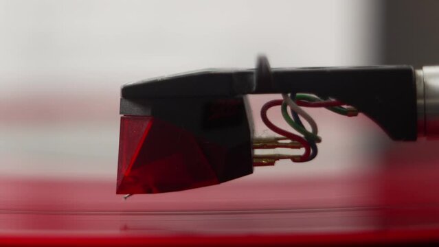Super close up of record player pick up being lifted up and down the groove of a red vinyl record