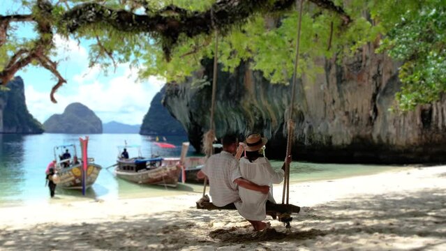 Koh Hong Island Krabi Thailand, a couple of men and women on a swing at the beach of Koh Hong, a tropical white beach with Asian women and European men in Krabi Thailand