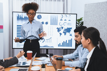 Young african businesswoman presenting data analysis dashboard on TV screen in modern meeting. Business presentation with group of business people in conference room. Concord