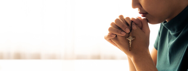 Praying female hand holding cross while praying to god faithfully. Concept of hope, religion,...