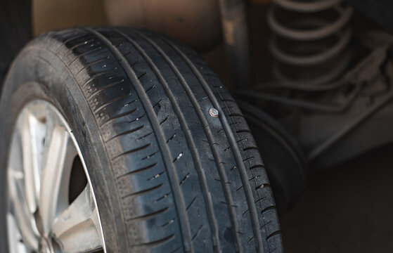 Close-up image of a car tire tread with a screw embedded in it, indicating a puncture risk..