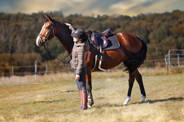 Horse stands with his rider on a meadow in the sun ready to ride out.