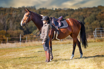 Horse stands with his rider on a meadow in the sun ready to ride out.