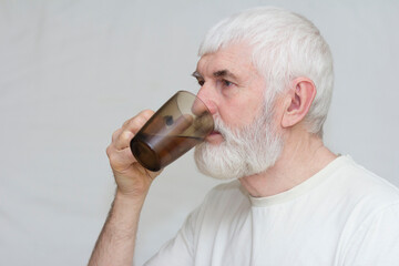 an elderly man with a gray beard drinks clean water from a glass