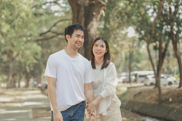 Happy young Asian couple in a park, Portrait of smiling couple near beautiful nature outdoors, lifestyle, Cheerful couple hugging each other, Young couple enjoying the sunny day at park
