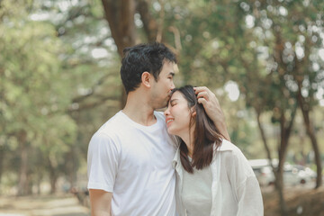 Happy young Asian couple in a park, Portrait of smiling couple near beautiful nature outdoors, lifestyle, Cheerful couple hugging each other, Young couple enjoying the sunny day at park