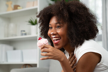 Funny African on mess face with whipped cream presenting cupcake topping on cherry in concept special pastel color. Content creating of social media with favorite sweets bakery dish. Tastemaker. - obrazy, fototapety, plakaty