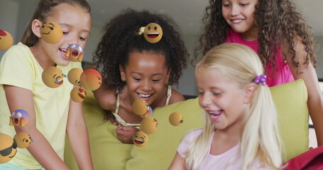 Image of various emojis moving over happy diverse schoolgirls using tablet together at beak time