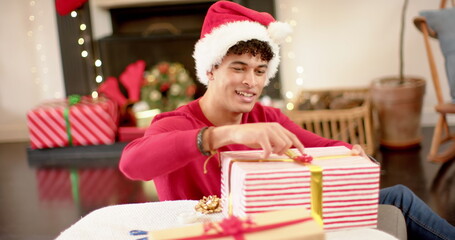 Obraz na płótnie Canvas Young biracial man wrapping gifts at home, with copy space