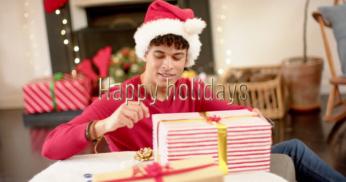 Image of happy holidays text over caucasian man wrapping christmas presents