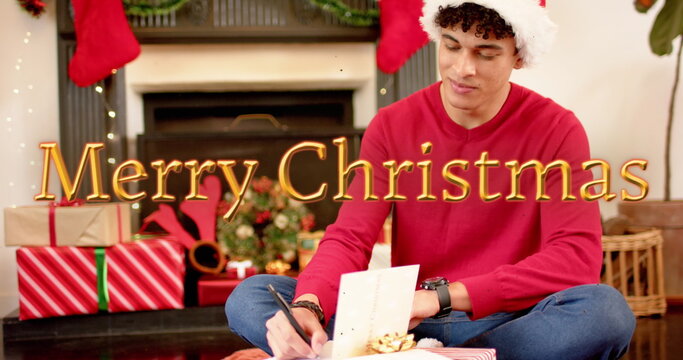 Image of happy holidays text over caucasian man writing christmas cards with presents