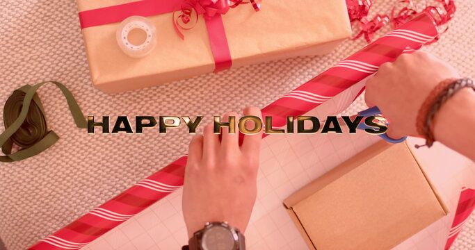 Image of happy holidays text over caucasian man wrapping christmas presents