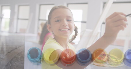 Fototapeta premium Image of paint pots over smiling caucasian schoolgirl painting in art class