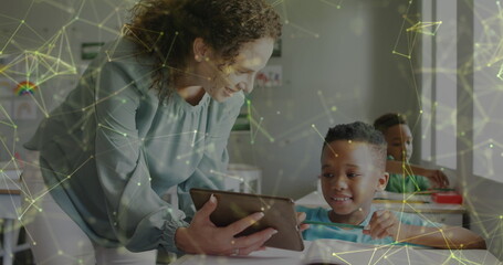 Image of networks over smiling diverse female teacher with tablet and schoolboy at desk in class